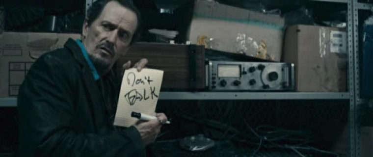 A man in front of radio equipment turns towards the reader with a peice of paper held up for the reader. The paper reads "Don't Talk."