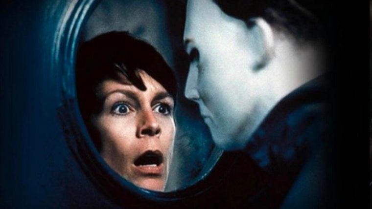 a surprised woman's face looks through a porthole style window at a man wearing a featureless white mask